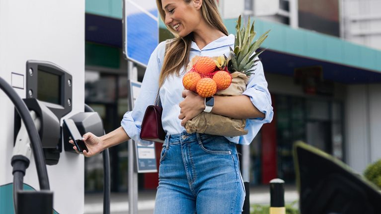 Happy young woman is charging an electric car in the parking lot - stock photo