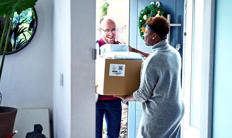 Delivery man handing over cardboard box to female customer during holiday season.