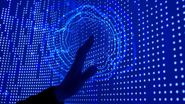 A hand reaching out to touch a deep blue screen covered in datapoint dots. A circular ripple effect emanates from the point of contact.